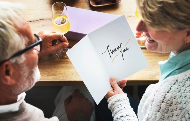 Senior couple enjoying wine - woman has greeting card with sentiment "Thank You"
