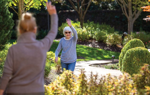 Two residents waving to each other outdoors.