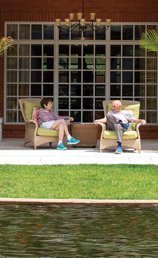 Two residents sitting on the patio across the pond talking.