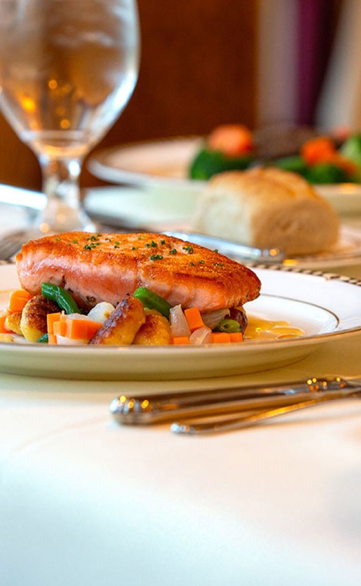 A fish dish on a fancy table with various wines.