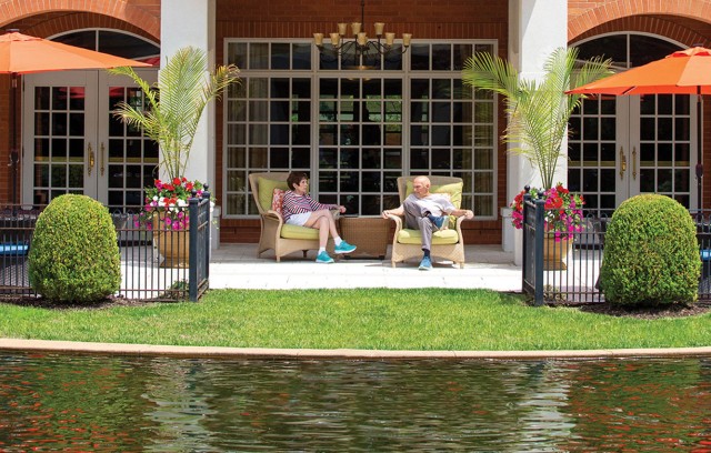 Two residents sitting on the patio across the pond talking.