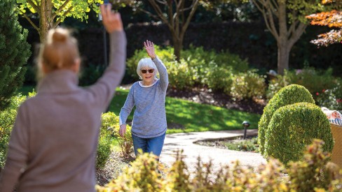 Two residents waving to each other outdoors.
