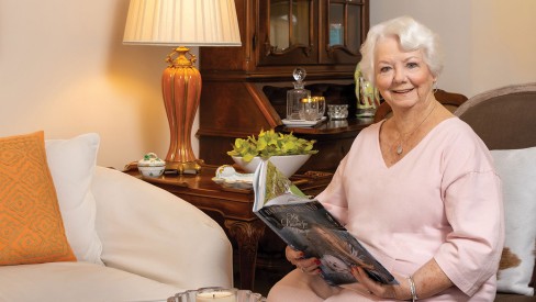 A woman sitting indoors with an open book smiling at the camera.