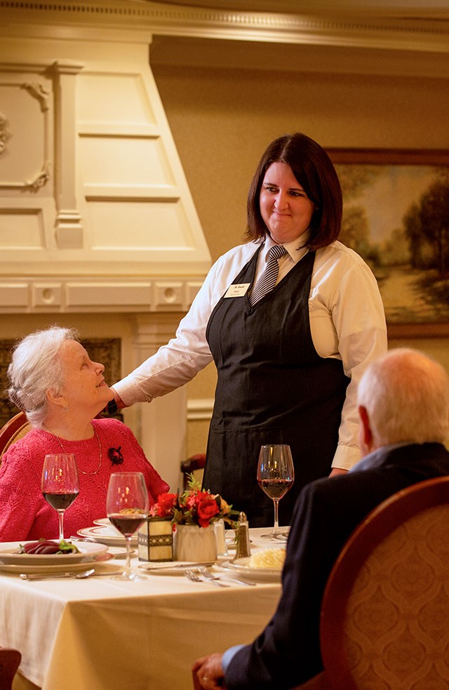 Team member standing and talking with four resident diners in the dining room.
